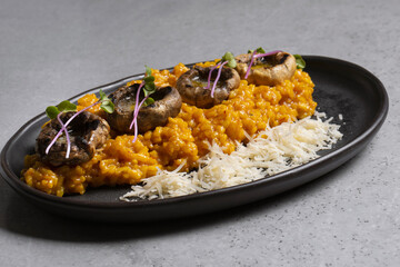 Pumpkin risotto with mushrooms and parmesan cheese on black plate