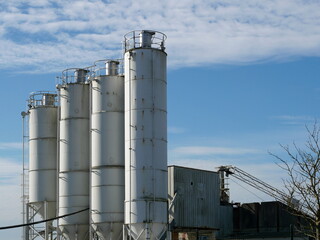 Multiple silos of a concrete plant rise into the sky. Industrial facility in a commercial area, essential for building materials. A technical and architectural motif.