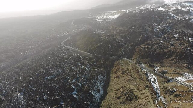Aerial view of beautiful volcanic landscape with highway and cars driving along snowy rocks. 4K drone video. Volcano Teide, Tenerife, Canary islands, Spain. Epic footage during dust storm calima