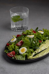 Fresh green salad with quail eggs, cherry tomatoes and guacamole in black plate on grey background
