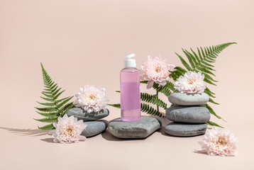 Bottle for cosmetics on a stone podium surrounded by fern leaves, chrysanthemum flowers.