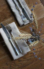 Dried wheat ear and blooming lavender with small flowers on the old wood table with served dining items. Vertical image for cozy mood table decoration

