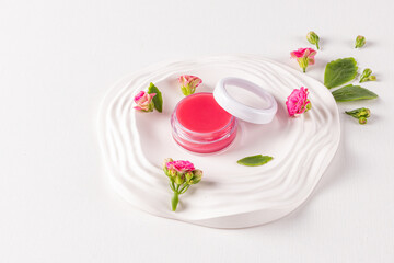 Open cosmetic jar with pink lip balm on a decorative tray among Kalanchoe flowers. The concept of moisturizing and nourishing the skin of the lips.