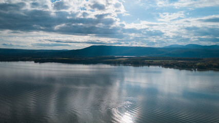 Aerial view of a vast lake reflecting clouds, surrounded by rolling hills and distant mountains.