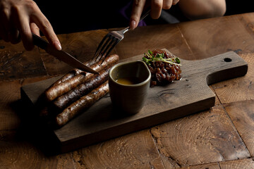Woman eating Grilled sausages with mustard and herbs on a wooden board