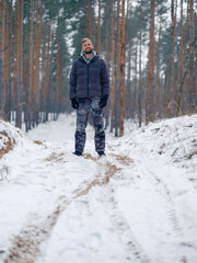 Naklejka premium Happy young smiling man walking on wood dirt road in snowy forest.