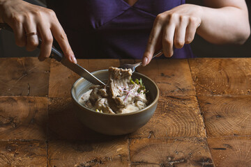 Woman eating rack of lamb in cream sauce with apple and radish in a bowl