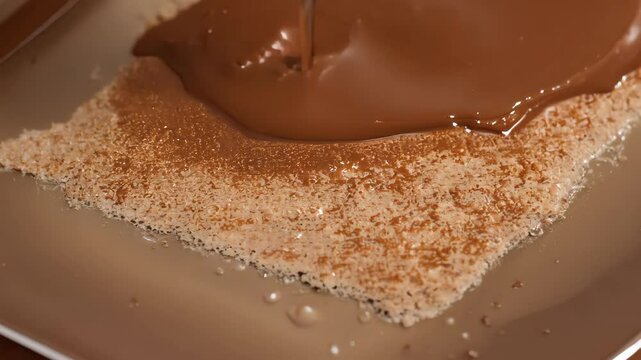 Rich chocolate sauce is poured on a delicately prepared dessert, creating a tempting treat.