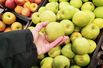 A woman holds a green apple in her hand. Buying fruits at the supermarket or at the market.