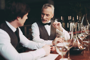 Confident elegant sommelier makes wine list in restaurant. Wine tasting.