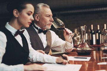 Experienced confident sommelier looks at glass of wine while sitting in restaurant. Wine tasting.