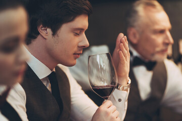 Confident handsome sommelier tasting wine in restaurant, holding glass in hand.