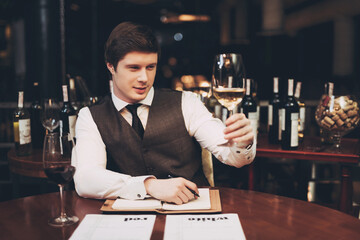 Young experienced sommelier tasting red wine, poured into glass, closing his eyes. Sommelier enjoys taste of alcoholic beverage.