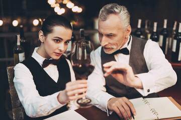 Old experienced sommelier tells young girl about specifics of taste of red wine in restaurant.