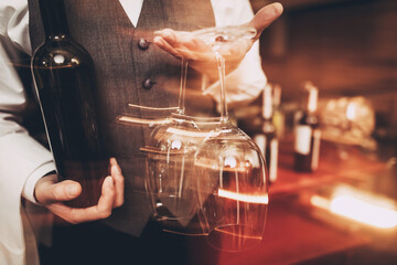 Close up. Sommelier in bow tie is holding with bottle of wine and wine glass. Blurred.
