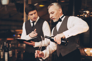 Two experienced sommeliers taste wine. Sommelier pours red wine from decanter into glass.