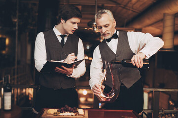 Two experienced sommeliers taste wine. Sommelier pours red wine from decanter into glass.
