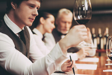 Confident handsome sommelier checks aging of wine at restaraunt. Wine tasting. Professional degustation expert in winemaking
