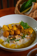 Bubur ayam, a traditional Indonesian food. Rice porridge with sliced chicken, rolled omelette, peanut, sambal (chili sauce), and kerupuk (crackers), poured with curry sauce. Served on wooden table