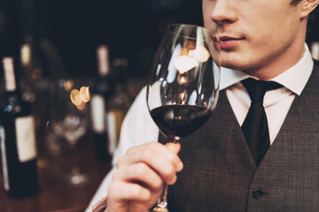 Close up. Confident handsome sommelier tasting wine in restaurant, holding glass in hand.