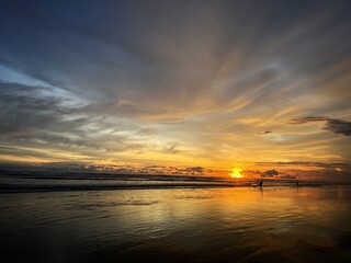 Obraz premium The natural beauty of the sunset on the beach, and the activity of fishermen looking for fish can be seen.