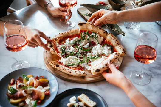 Friends enjoy a dinner party with pizza and rose wine in a bar or a restaurant.