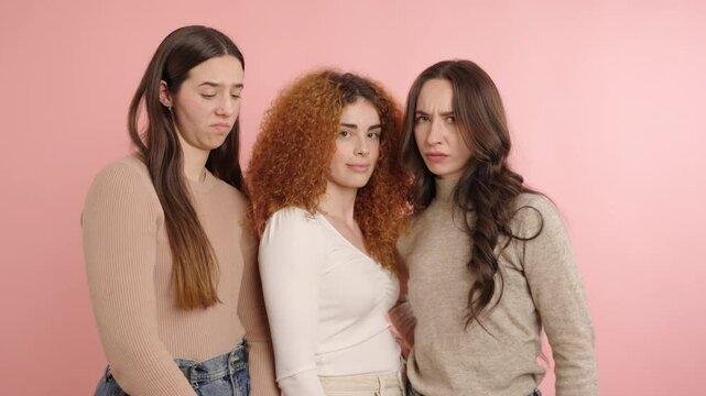 Three young women showing disgust expressions on pink background
