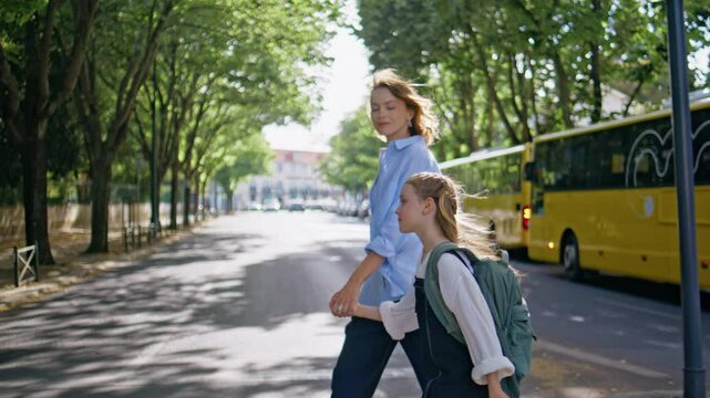 Carefree family crossing road. Mother little daughter walking greenery alley