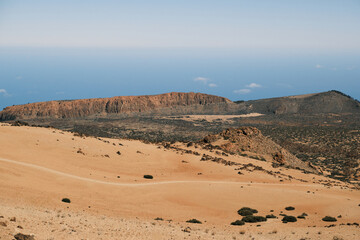 Stunning panoramic view of a volcanic landscape. Sandy dunes meet rugged, rocky terrain under a clear blue sky. Ideal for travel, nature, and geology projects.