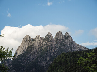 Dramatic rocky mountain peaks with patches of snow, set against a cloudy sky. The rugged terrain and towering cliffs create a striking contrast with the soft clouds above.