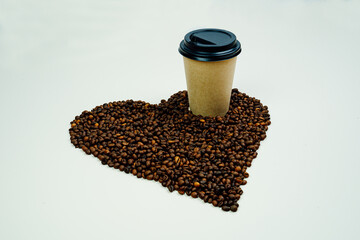 Naklejka premium Heart made of coffee beans. Paper mug with coffee stands on coffee beans. 