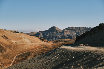Serene desert landscape. Winding dirt road leads through sun-drenched mountains under a clear blue sky. Perfect for travel, adventure, and nature themes.