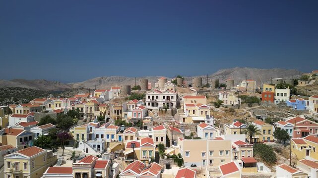 colorful houses over hill with blue waters and mountains in the background on the Greek Symi island