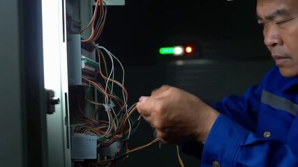 A male electrician working on a switchboard in overalls, with emergency lighting providing the backdrop