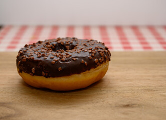 A freshly baked chocolate donut adorned with crunchy chocolate sprinkles rests on a wooden surface, showcasing its glossy glaze and inviting appearance