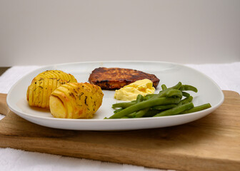 Juicy grilled pork chop is paired with crispy hasselback potatoes and fresh green beans, all garnished with a dollop of garlic butter on a wooden cutting board