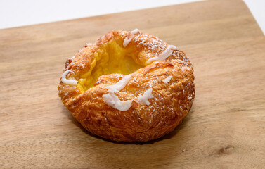 A warm, flaky pastry rests on a wooden board, revealing a creamy filling topped with a light drizzle of icing, inviting a delightful taste experience