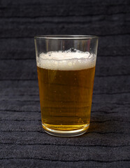 A clear glass filled with beer, exhibiting a foamy top and bubbles rising throughout. The dark background highlights the drink's vibrant color