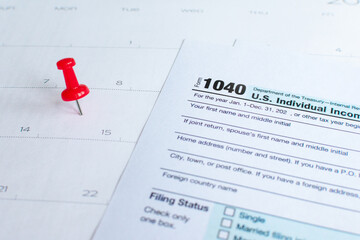 Close up shot of a red drawing pin (thumbtack or pushpin) on a calendar on the 15th. With Form 1040...