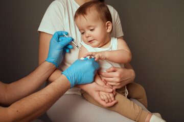 A healthcare provider gives a vaccination to a young child seated on a mother's lap. The provider...