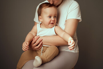 A joyful baby sits comfortably on a parent's lap, wearing a white tank top and light brown pants