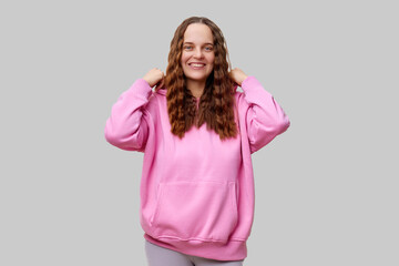 A young woman with wavy hair is smiling confidently while wearing a pink hoodie. She stands against...