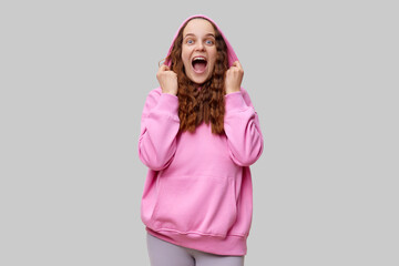 A young woman with curly hair enthusiastically smiles and poses in a pink hoodie. Her joyful...