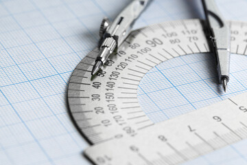 Protractor and compass on blue graph paper.