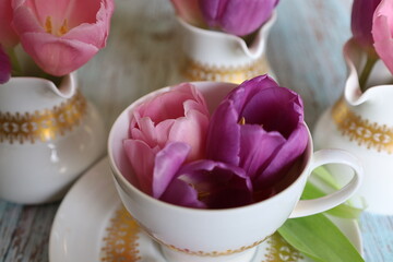 On the wooden table, there is a cup filled with purple tulip flowers and three milk jugs with tulips. Easter Table Decoration. Springtime decor. Close up