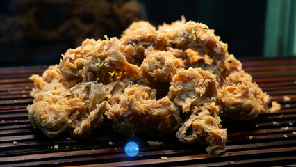 A close-up of crunchy fried chicken drumsticks and thighs, served fresh from the fryer at a local street vendor stall. The crispy coating enhances the rich flavor