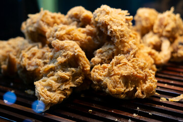 Freshly fried crispy chicken with a crunchy golden texture, displayed on a wooden rack at a street vendor's stall. A popular fast food option for hungry customers