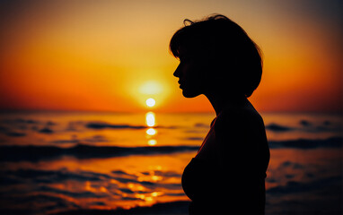 A woman’s silhouette standing by the ocean, watching the sunset