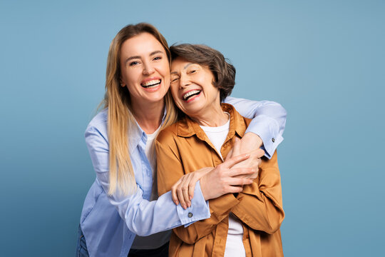 Happy mother and daughter embracing and smiling on blue background