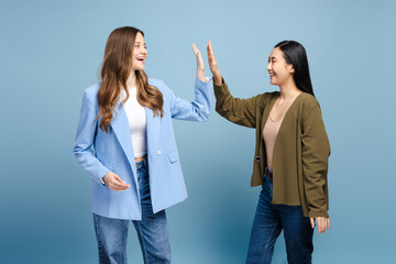 Two happy businesswomen giving high five celebrating success on blue background